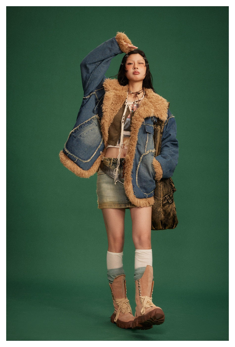 Model wearing the open navy denim jacket with tan fleece-like collar and cuffs, a cropped top, denim skirt and boots, on