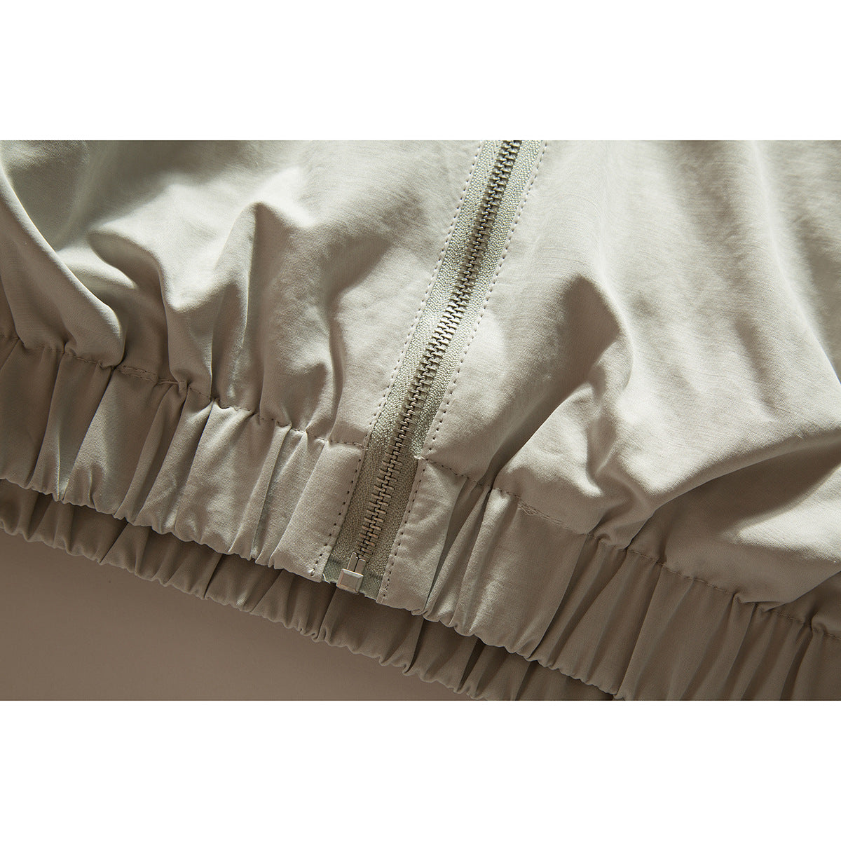 Close-up of a light beige jacket's front zipper and gathered elastic hem.