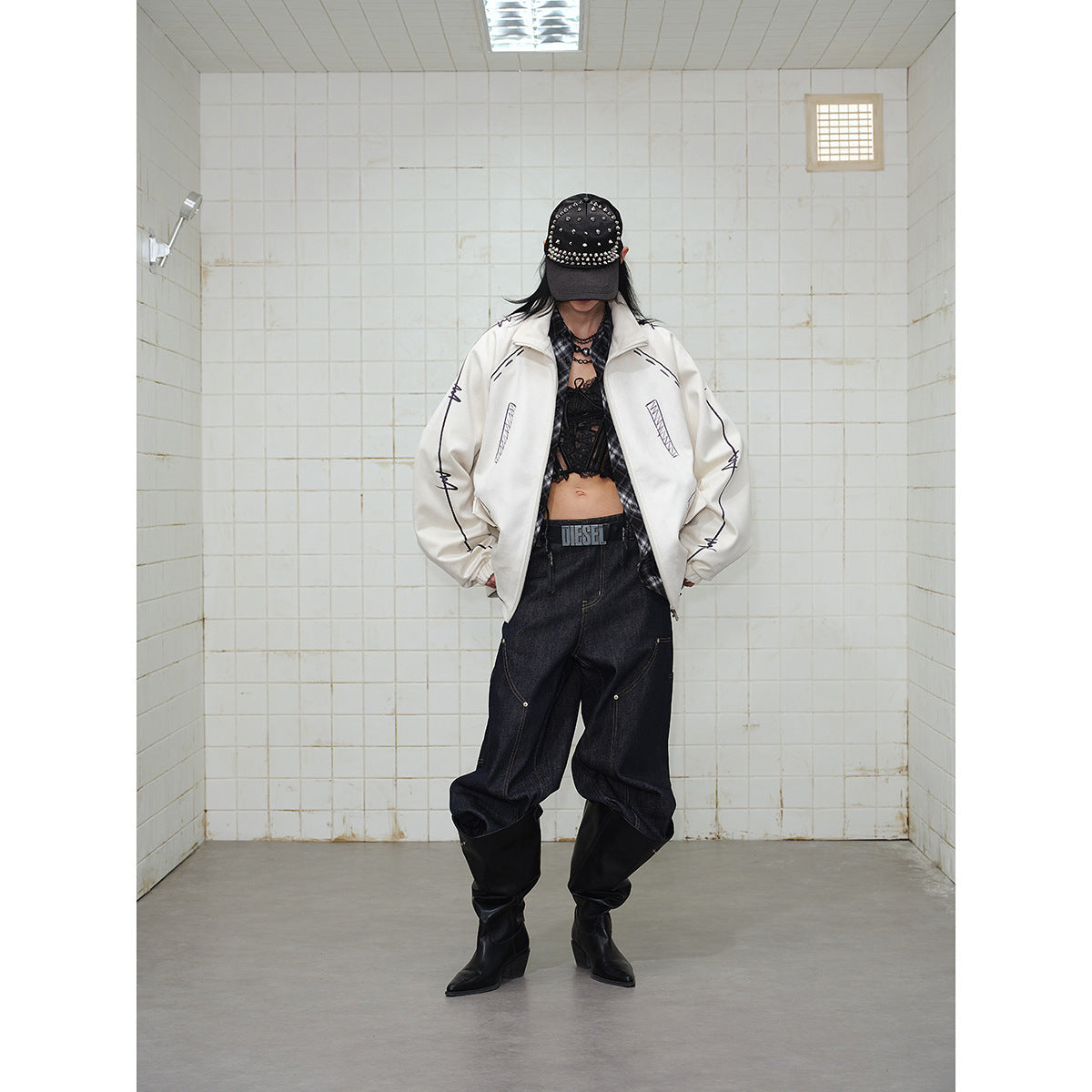 Model wearing a cream zip jacket with black sketch-like graphics, dark baggy jeans, a black studded cap and boots.