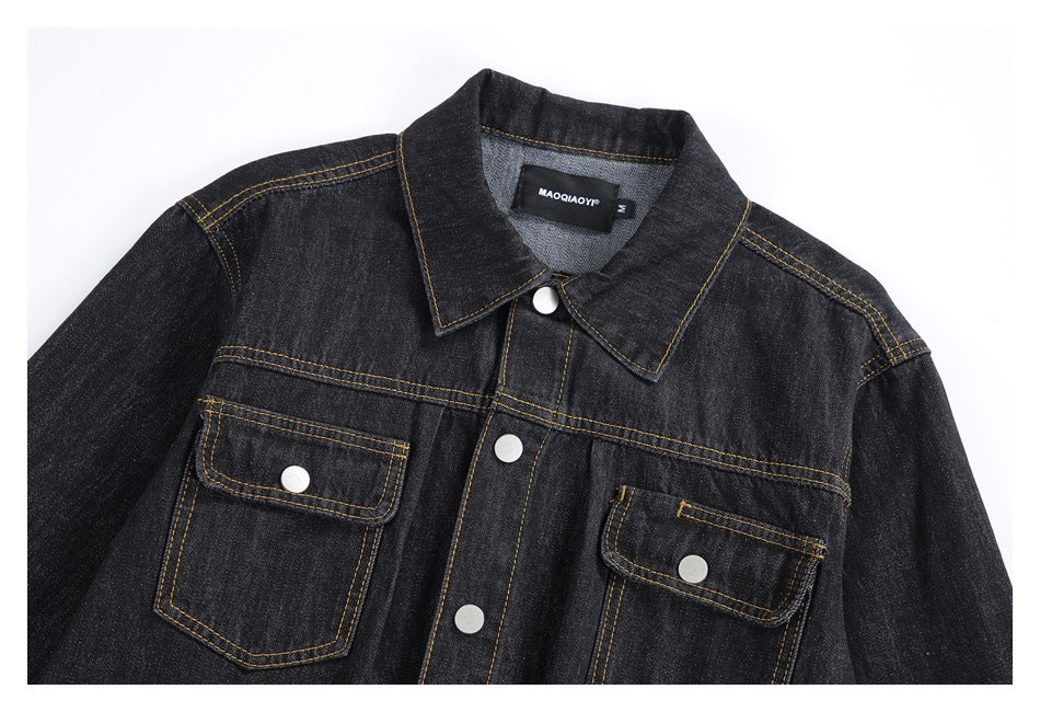Close-up of the black denim jacket's front, showing its pointed collar, snap buttons, and two flap pockets.
