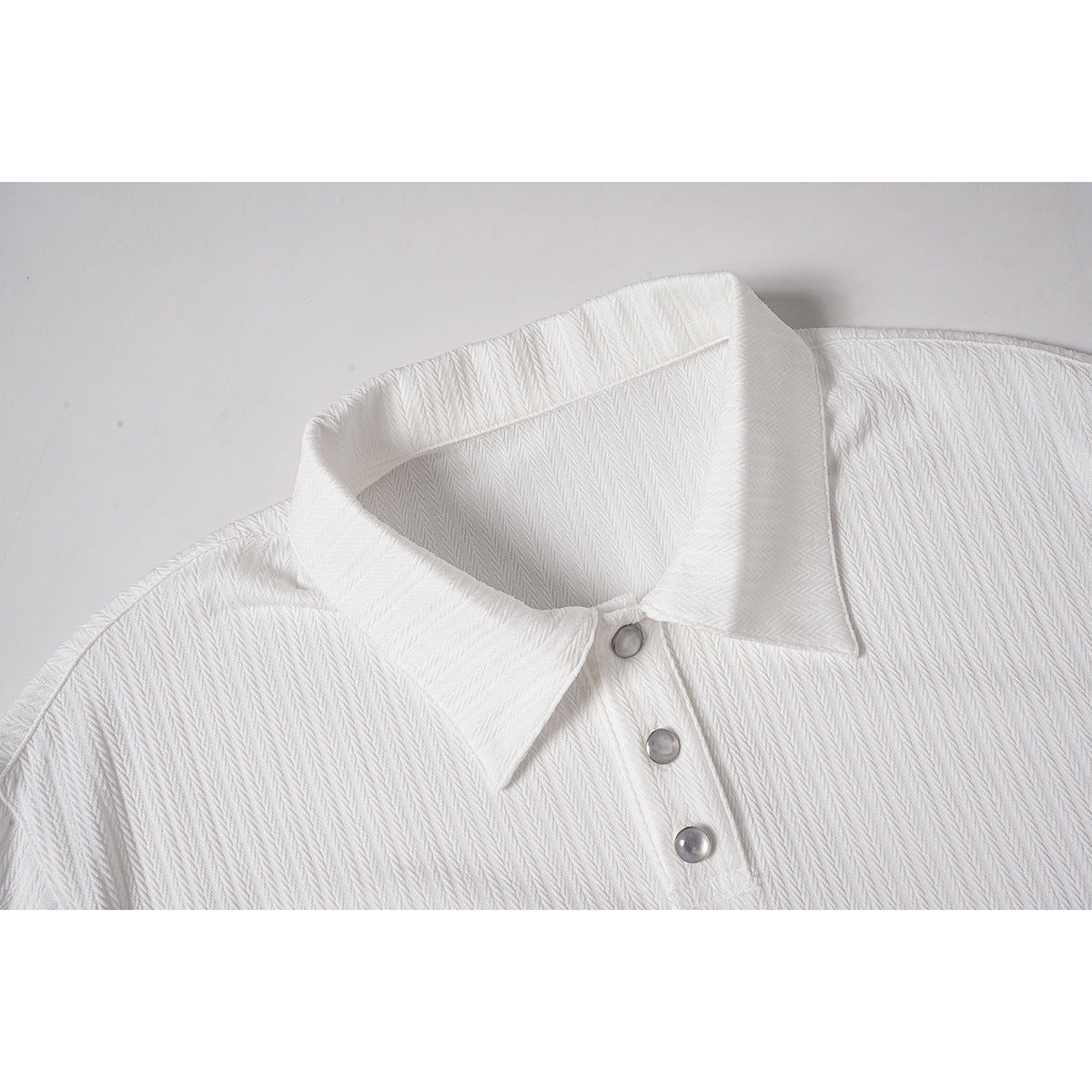Close-up of a white polo shirt's pointed collar and three gray buttons, showing a subtle textured pattern.