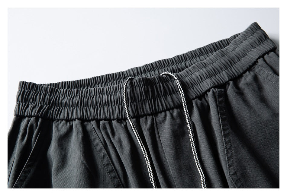 Close-up of charcoal pants showing the gathered elastic waistband, white drawcord, and front pocket seam.