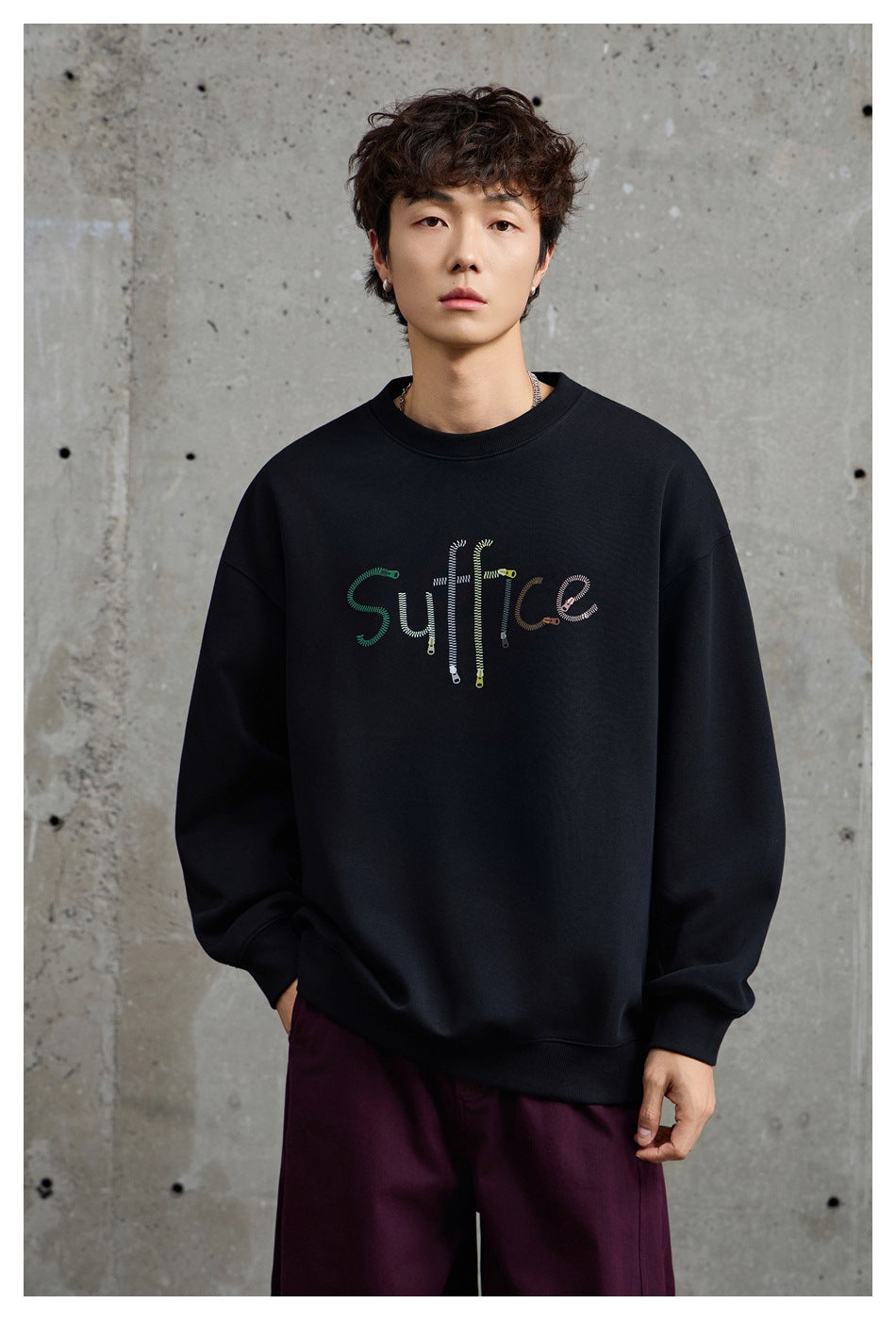 Close front view of a model wearing a black crewneck sweatshirt with colorful embroidered lettering.