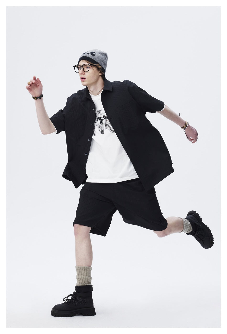 Model in a black short-sleeve button-up shirt and matching shorts, shown in a dynamic pose.