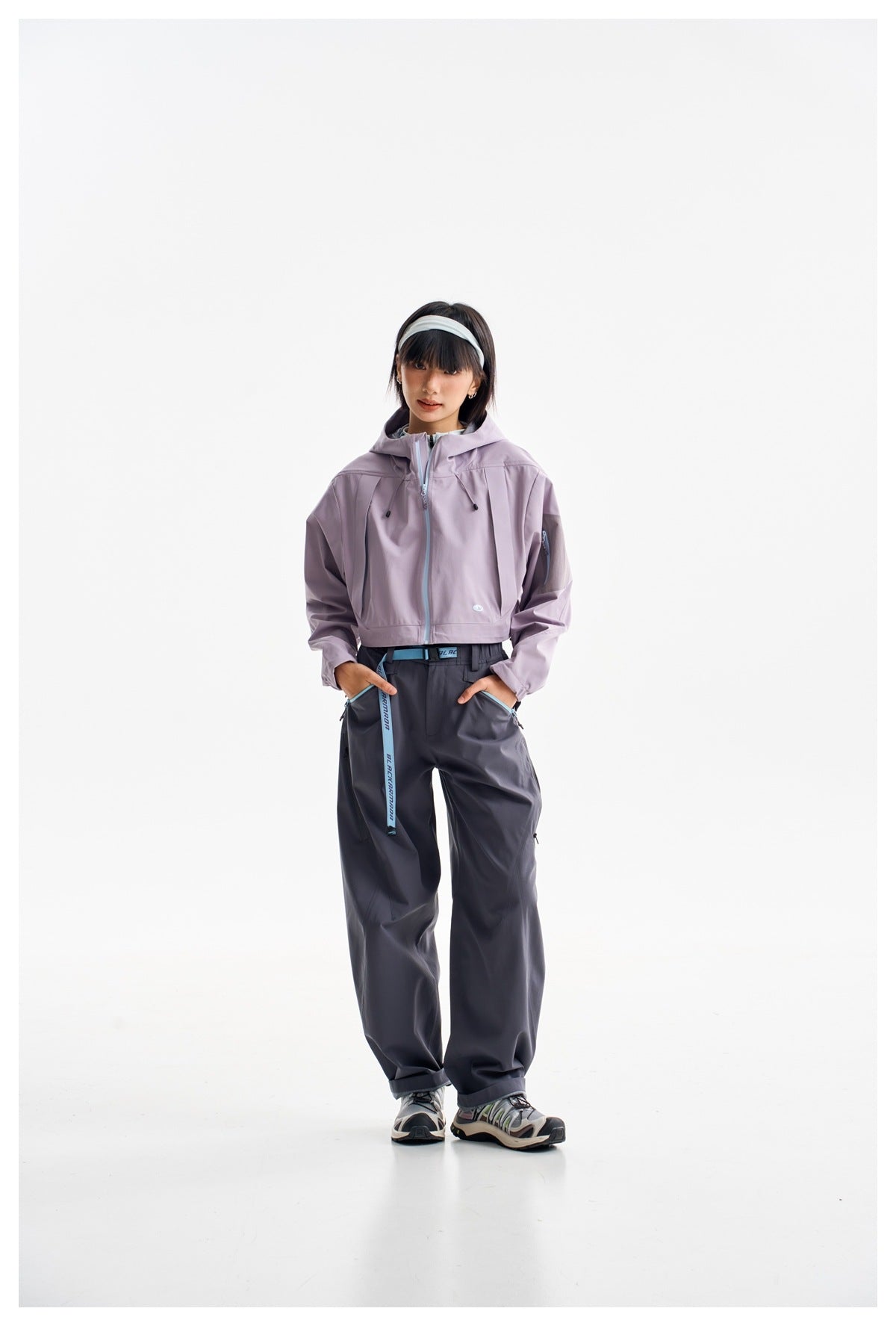 Front view of a model in a lavender cropped hooded jacket and dark loose trousers against a white background.