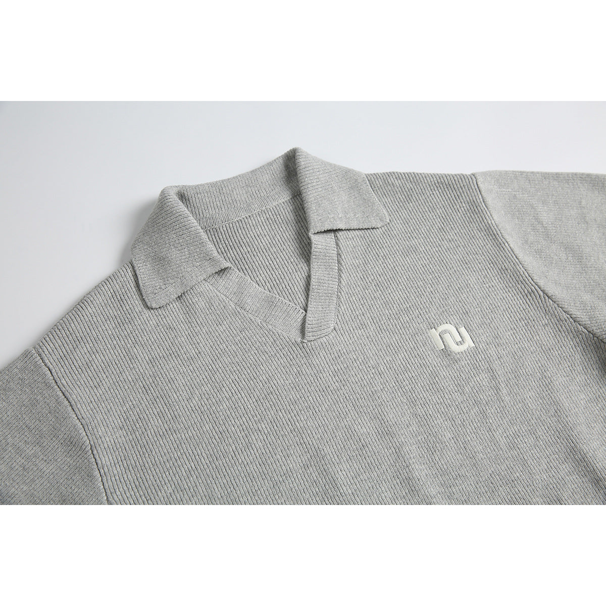 Close-up of a light gray ribbed sweater's notched collar and chest with a small white embroidered emblem.