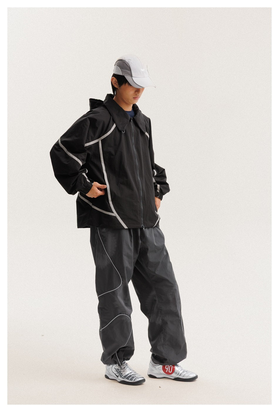 Angled view of a model wearing a black jacket with pale curved piping and dark pants.