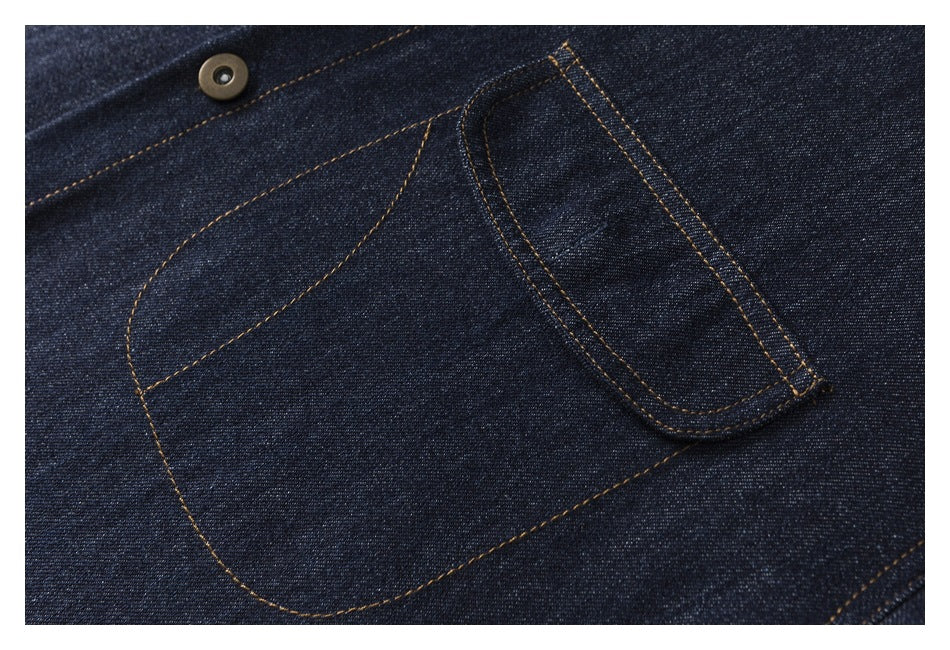 Close-up of the shirt's curved chest pocket, flap and button against dark indigo denim with contrast stitching.