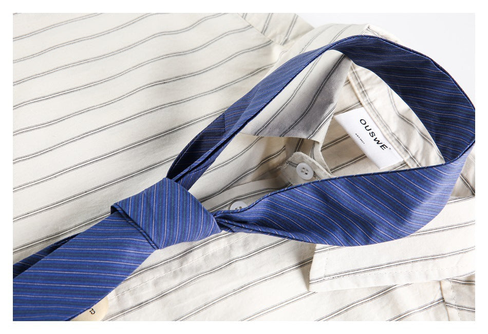 Close-up of a blue striped tie knotted over the collar of a cream shirt with thin dark stripes.