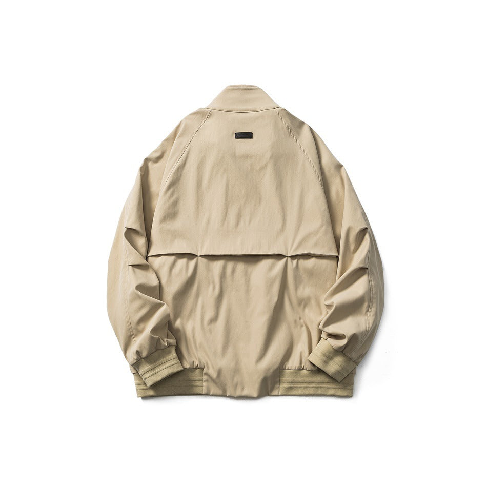 Back view of light khaki jacket flat lay showing raglan sleeves, back yoke seam, small dark patch and ribbed hem