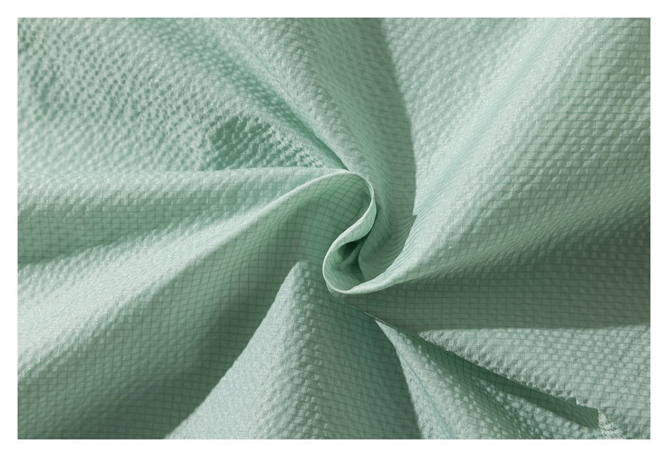 Close-up of pale mint-green fabric arranged in folds, showing a fine square grid texture.