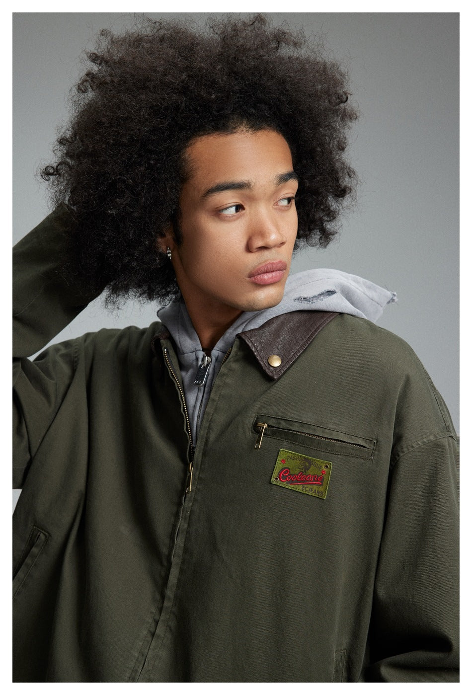 Model wearing an olive jacket with a dark brown contrast collar, zip chest pocket and gray hoodie.
