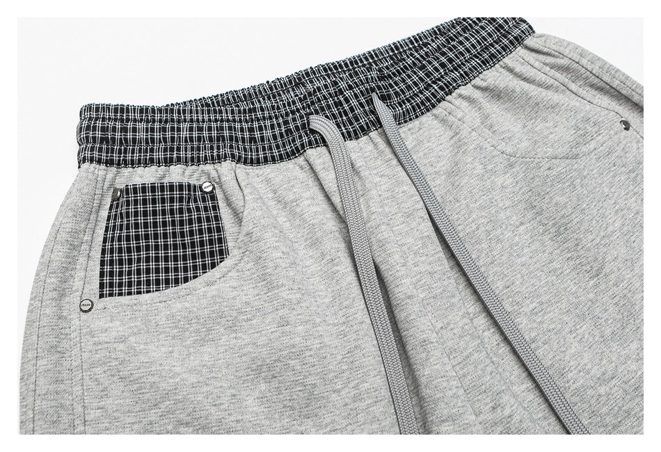 Close front view of heather-gray pants with a black-and-white plaid waistband and pocket panel, plus gray drawstrings.