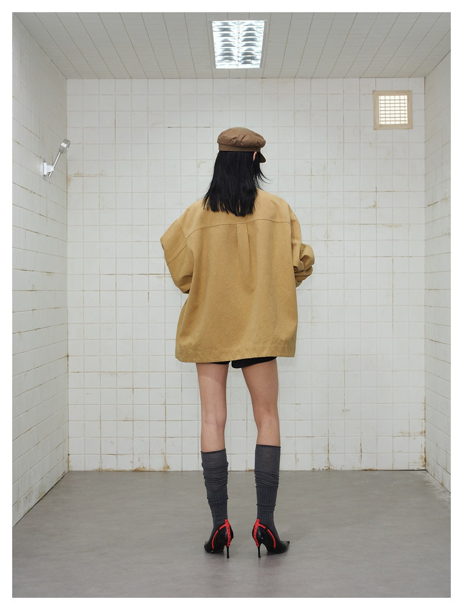 Back view of a model wearing an oversized tan jacket, brown cap, gray socks, and black heels.