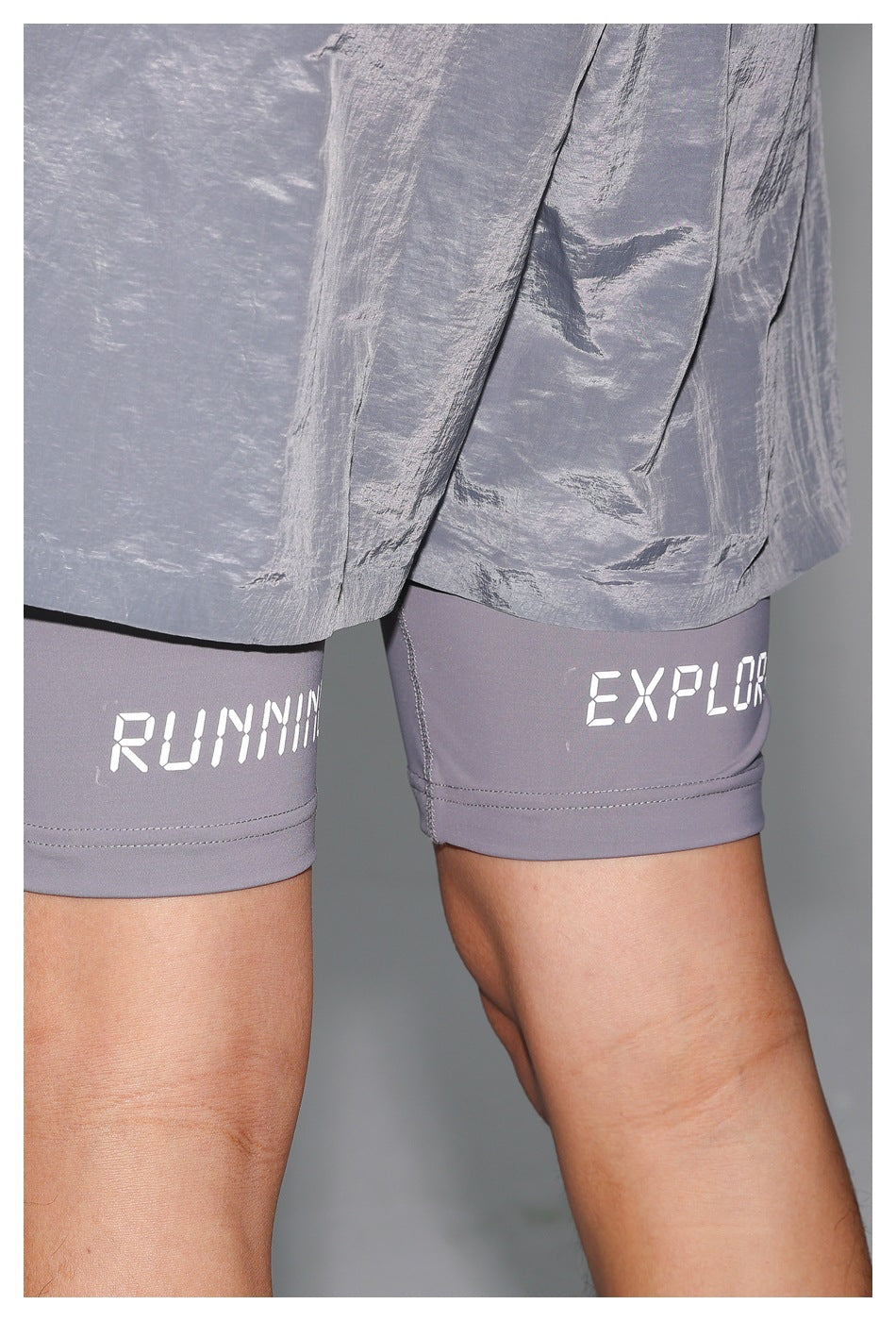 Close-up of pale blue-gray shorts over gray compression shorts with white lettering printed on the leggings.