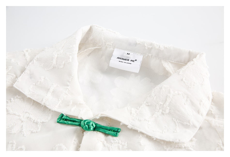 Close-up of a white floral shirt's collar, green frog closure, and sewn-in neck label.