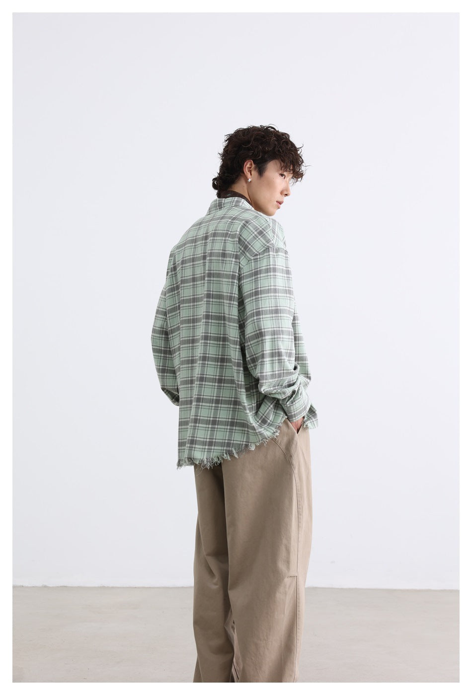 Back-side view of a model wearing a sage green plaid button-up shirt with a frayed hem.