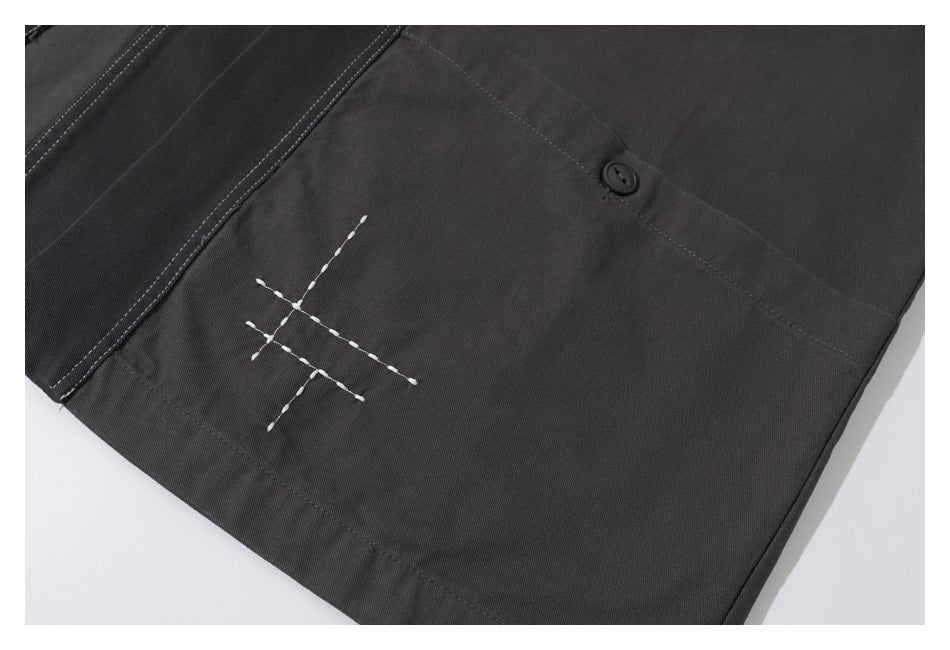 Close-up of a dark charcoal garment showing white crossed stitching, a seam, and a dark button.