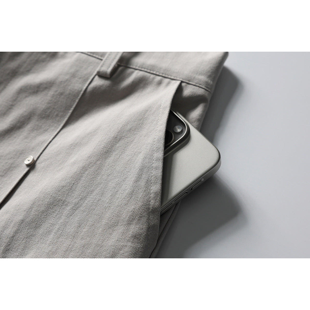 Close-up of a phone tucked into the pocket of light gray herringbone trousers.