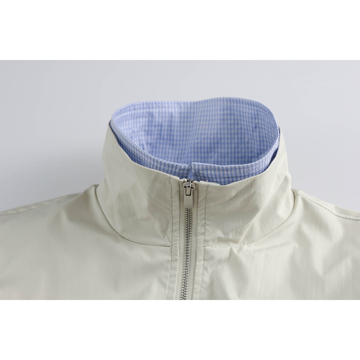 Close-up of an ivory jacket's raised collar, blue checked lining and front zipper.