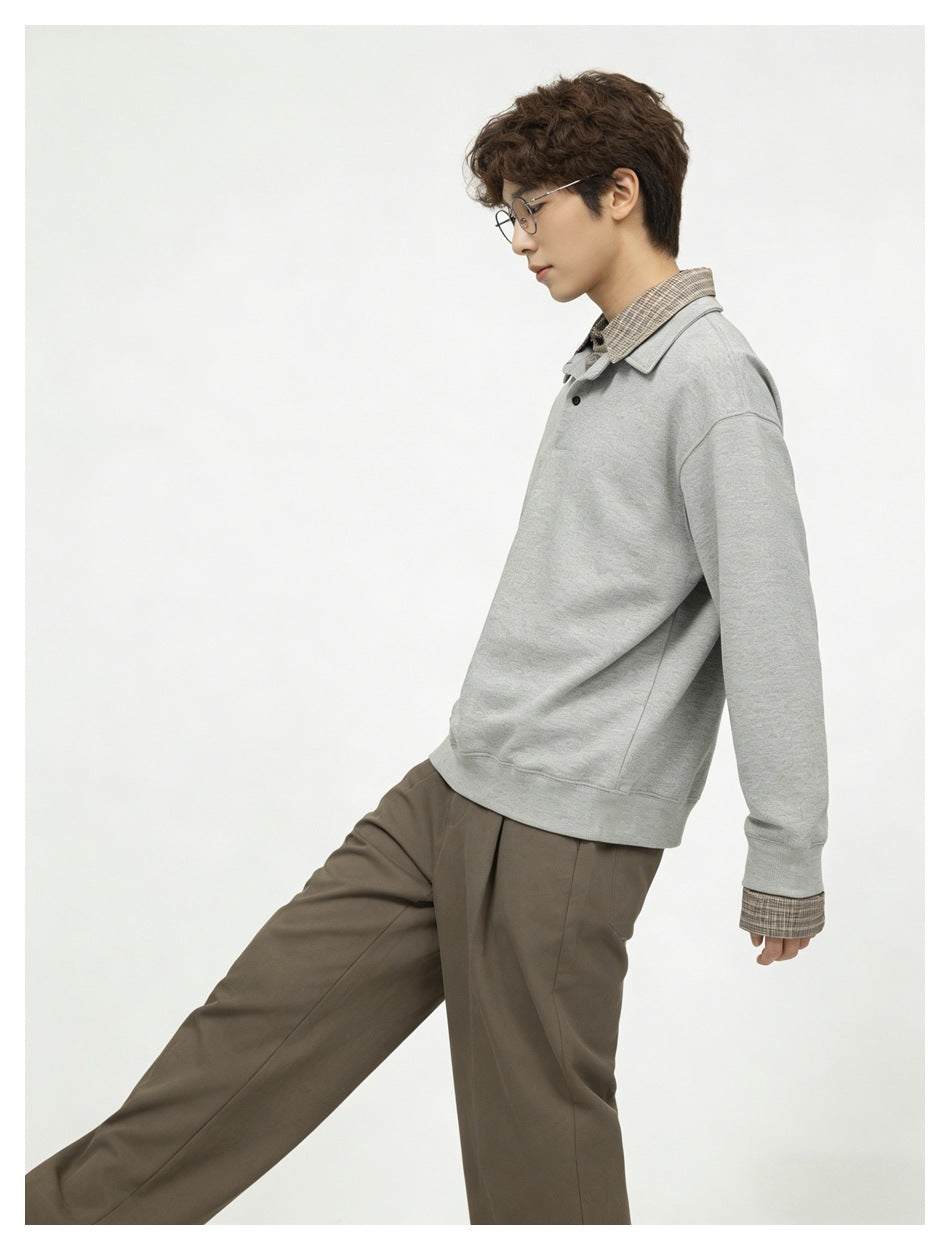 Side view of model in gray sweatshirt with plaid collar and cuff layers, with olive-brown pleated trousers