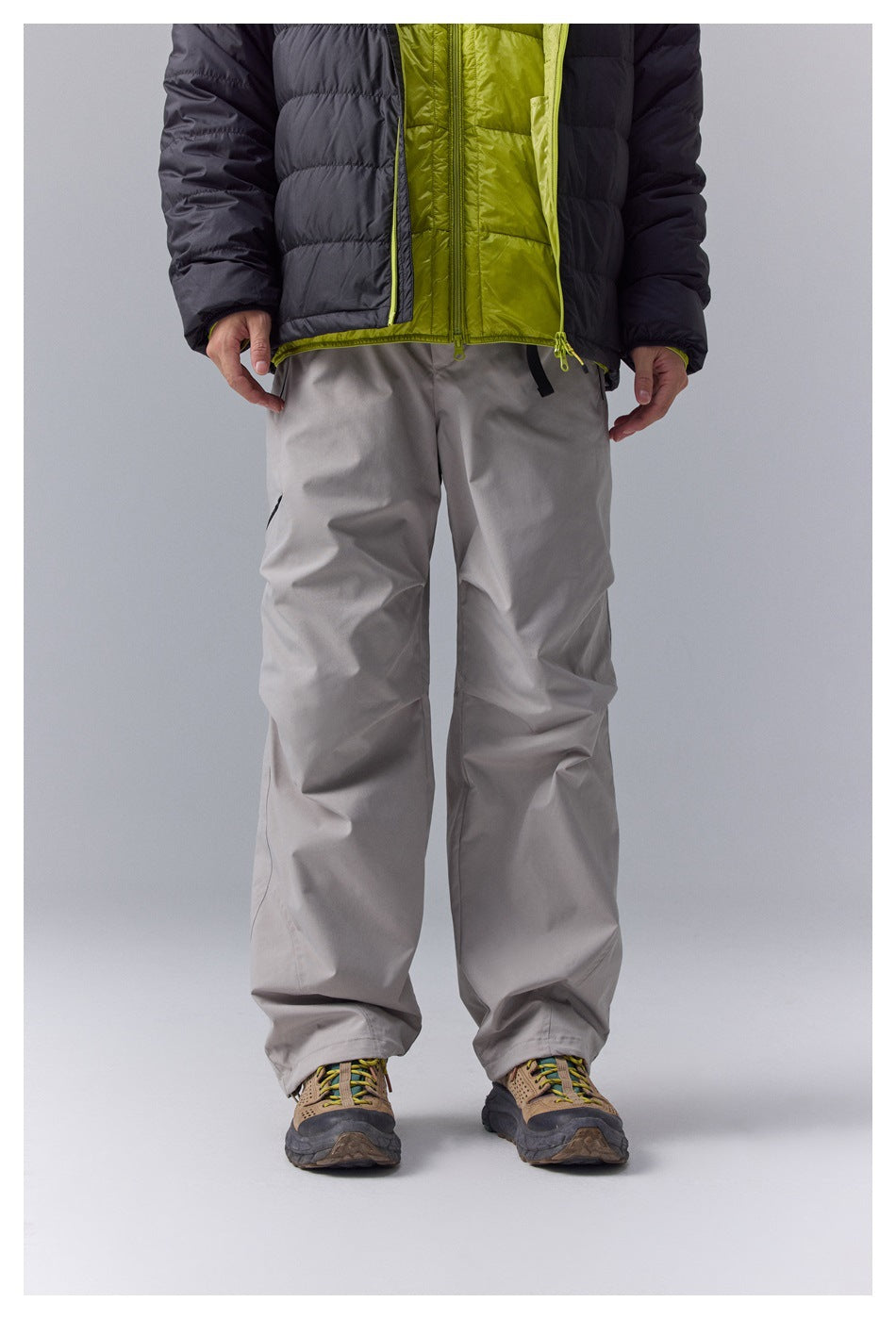 Front view of loose-fit light gray pants worn with a black jacket featuring a lime-green inner layer.