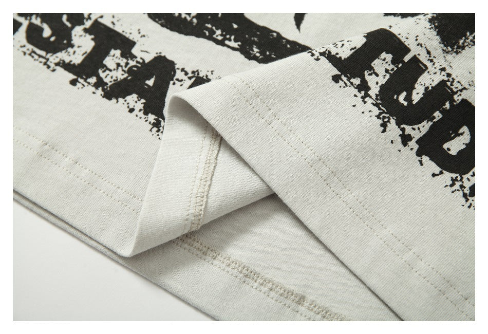 Close-up of an off-white T-shirt with a black distressed graphic and folded, stitched hem.