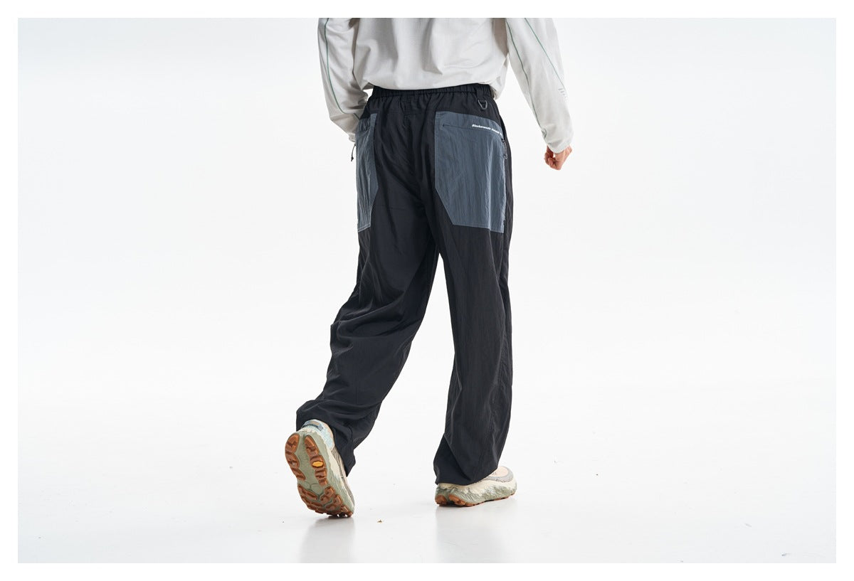 Rear view of a model wearing loose black pants with gray-blue back pocket panels and an elastic waistband.