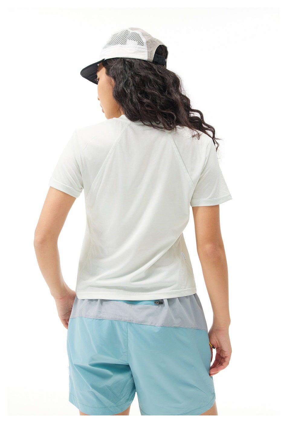 Rear view of a model wearing a white short-sleeve shirt, light blue shorts, and a white mesh cap.