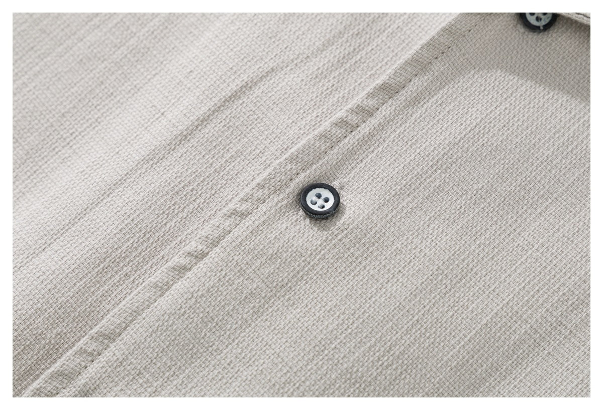 Close-up of the light beige shirt's textured fabric and dark-edged buttons.