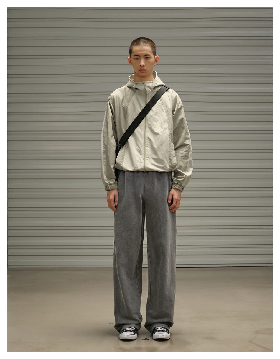 Model standing front view in loose gray washed sweatpants with a light hooded zip jacket and black sneakers