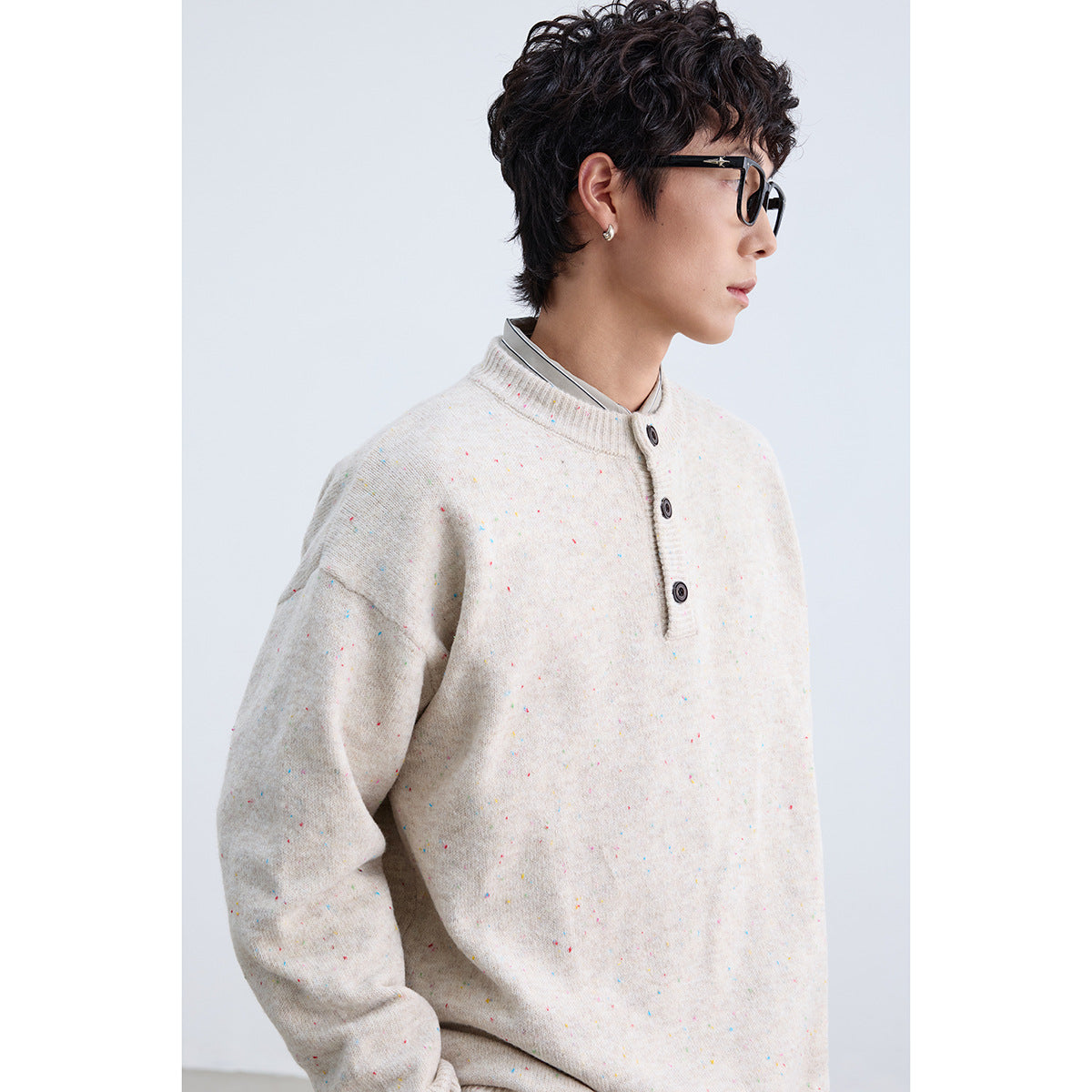 Close-up side view of a model wearing a cream speckled knit sweater with a ribbed collar and three-button placket.