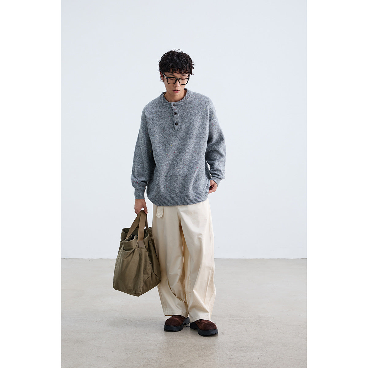 Full-length model wearing a gray multicolor-speckled knit sweater with a three-button placket and cream trousers.