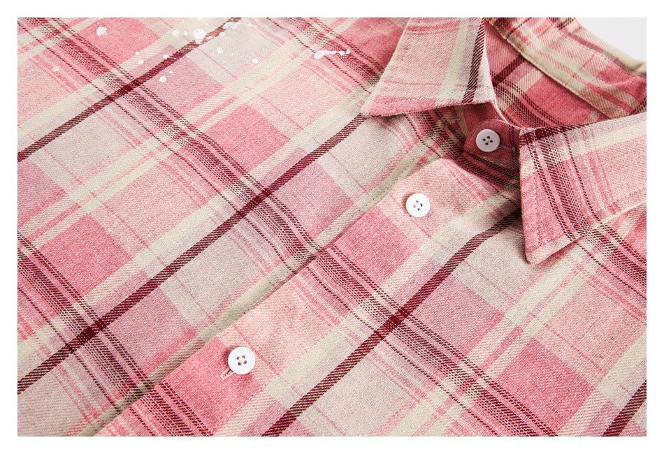 Close-up of a pink, cream, and burgundy plaid shirt front with a pointed collar and white buttons.