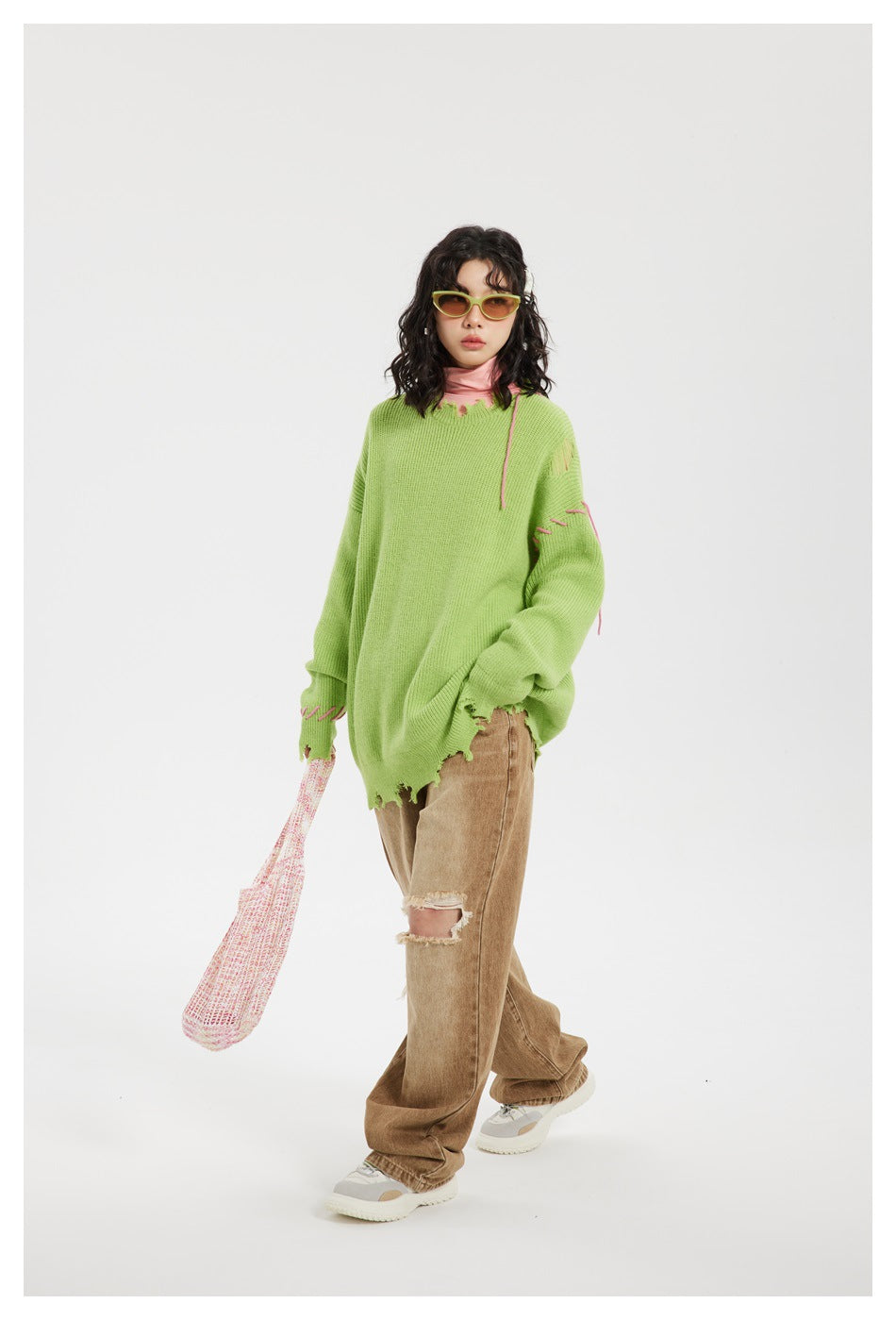 Front view of a model wearing an oversized lime-green sweater with pink stitched accents and a distressed hem.