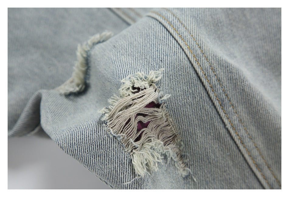 Close-up of light blue denim with a frayed, ripped patch and tan double stitching.