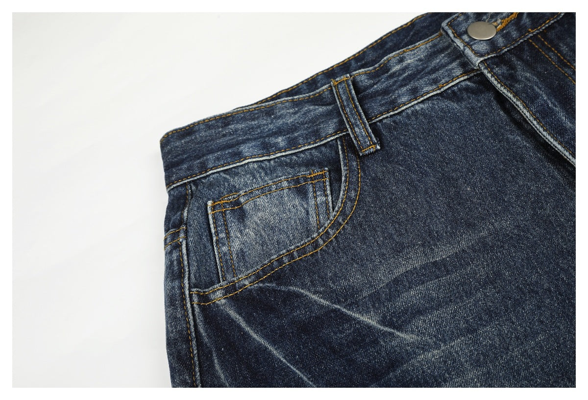 Close-up of dark blue jeans showing the waistband button, belt loop, and front pocket with golden stitching.