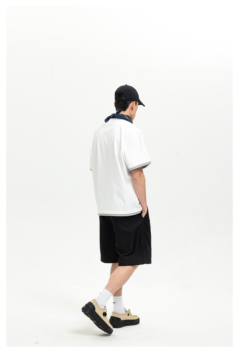 Rear view of a model wearing a white shirt with gray sleeve and hem trim, black shorts, and a black cap.