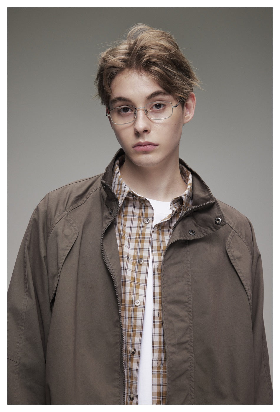 Close-up of a brown jacket with a stand collar and snap details, layered over a checked shirt.
