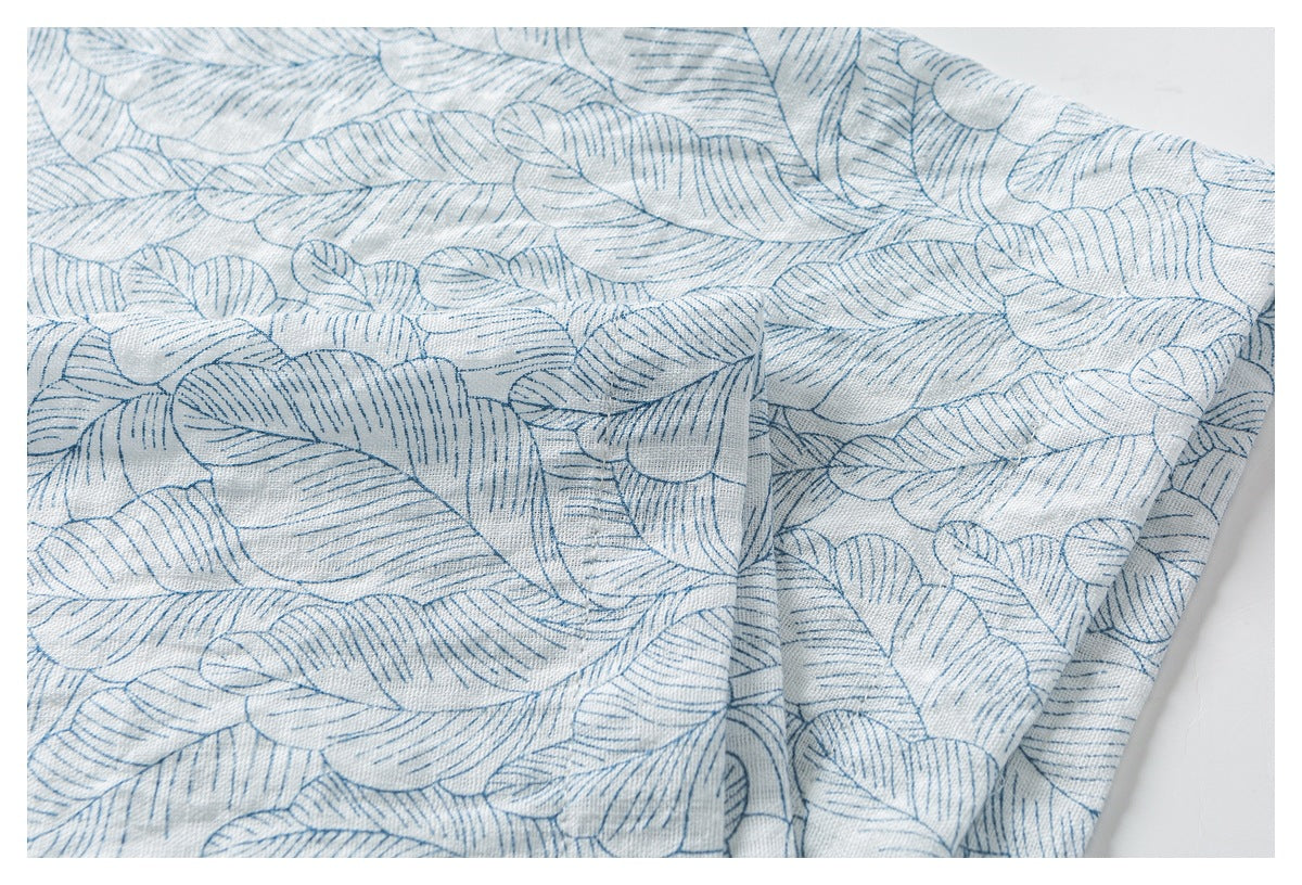 Close-up of pale blue-gray fabric with an allover pattern of blue outlined leaves, softly folded.