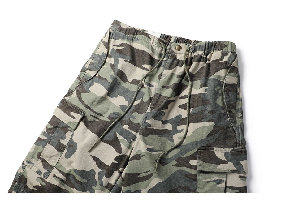 Close front view of camouflage cargo pants with an elastic waist, drawcords and flap pockets.