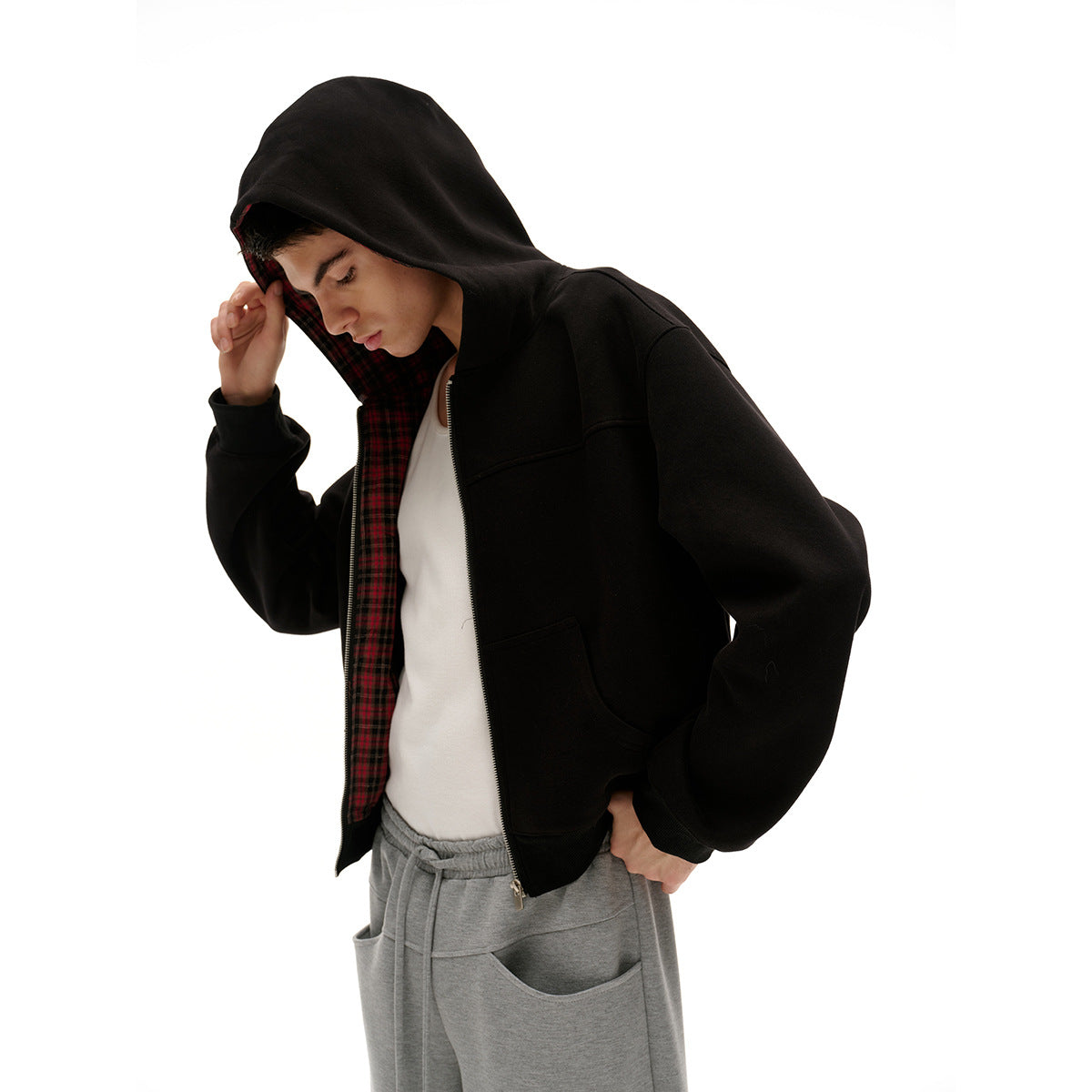 Model wearing a black zip-up hoodie with red plaid hood lining and gray sweatpants, shown close up against white.