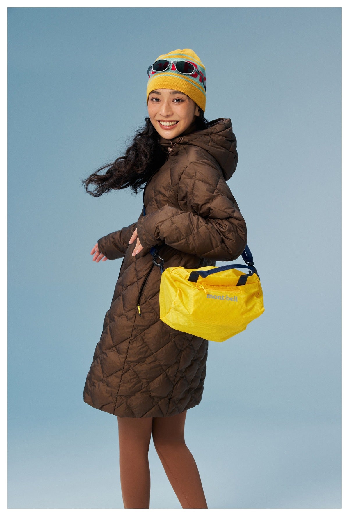 Model wearing a brown quilted hooded coat with a yellow crossbody bag.