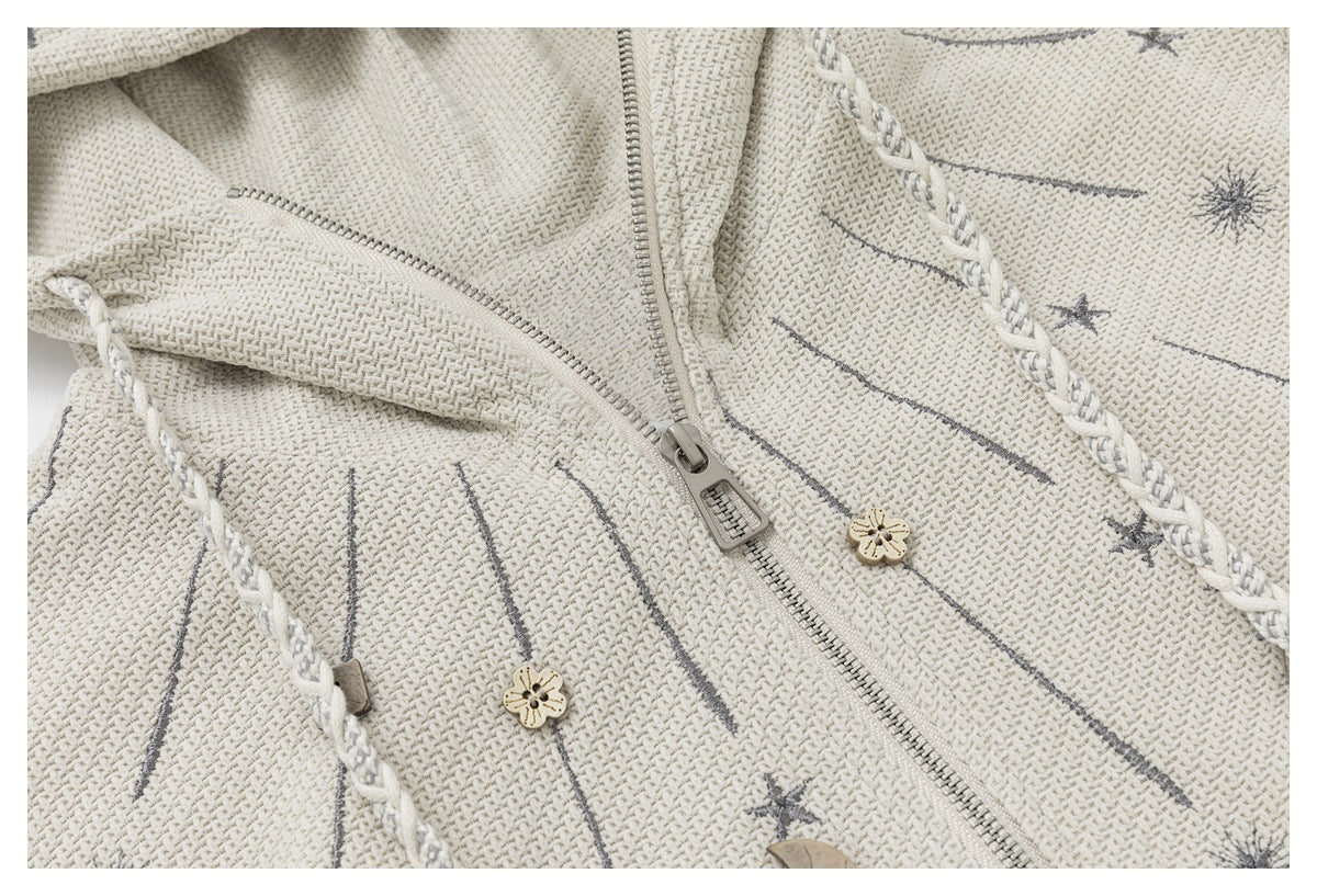 Close-up showing the ivory jacket's zipper, textured surface, braided trim, and small decorative buttons.