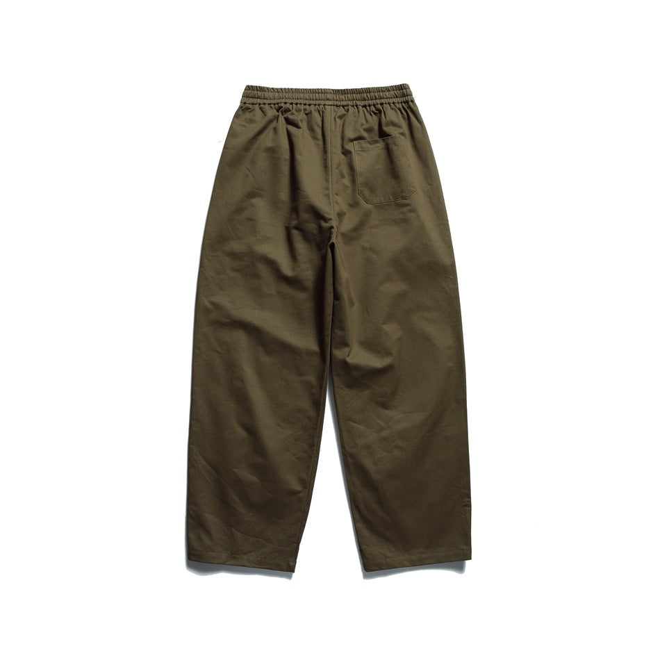 Back view of loose-fit olive trousers with an elastic waistband and a single patch pocket.