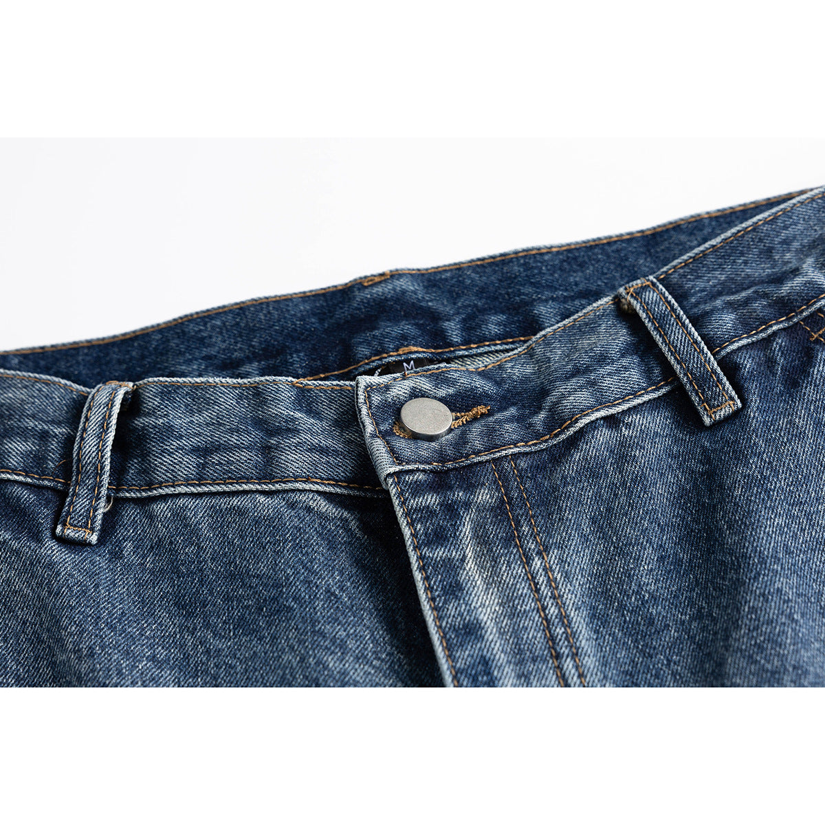 Close-up of blue washed denim jeans showing the waistband, belt loops, metal button and fly stitching.