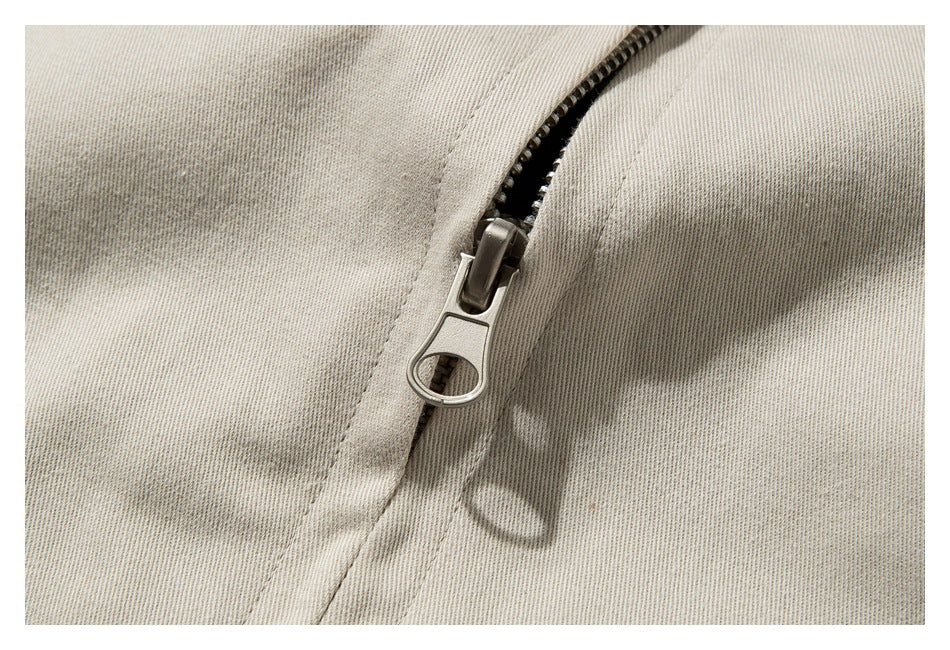 Close-up of a metal zipper and stitching on beige garment fabric.