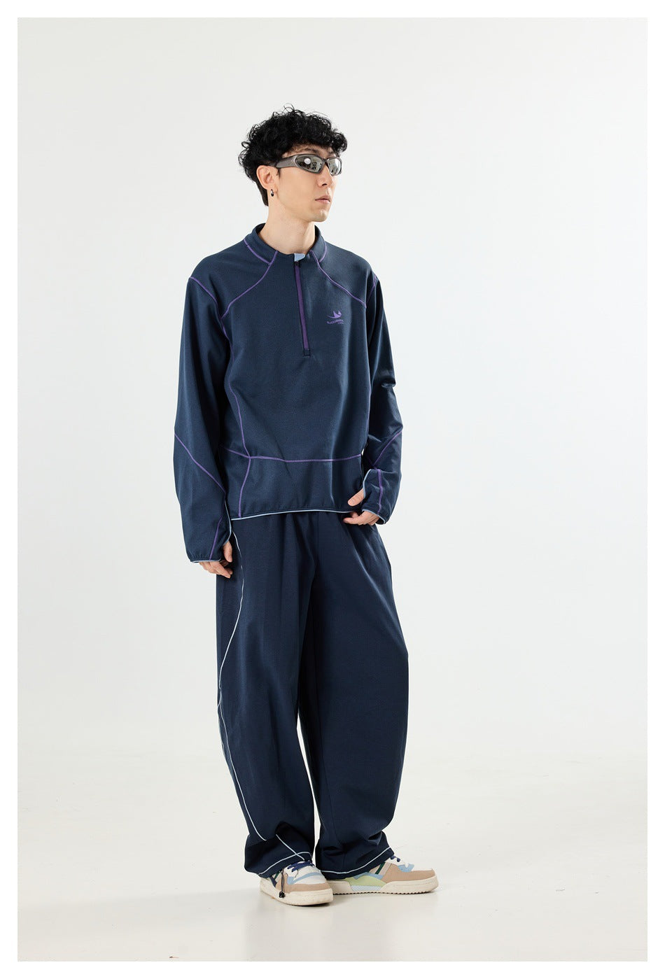 Model wearing a navy quarter-zip top with purple seam details and matching loose pants, shown from the front.