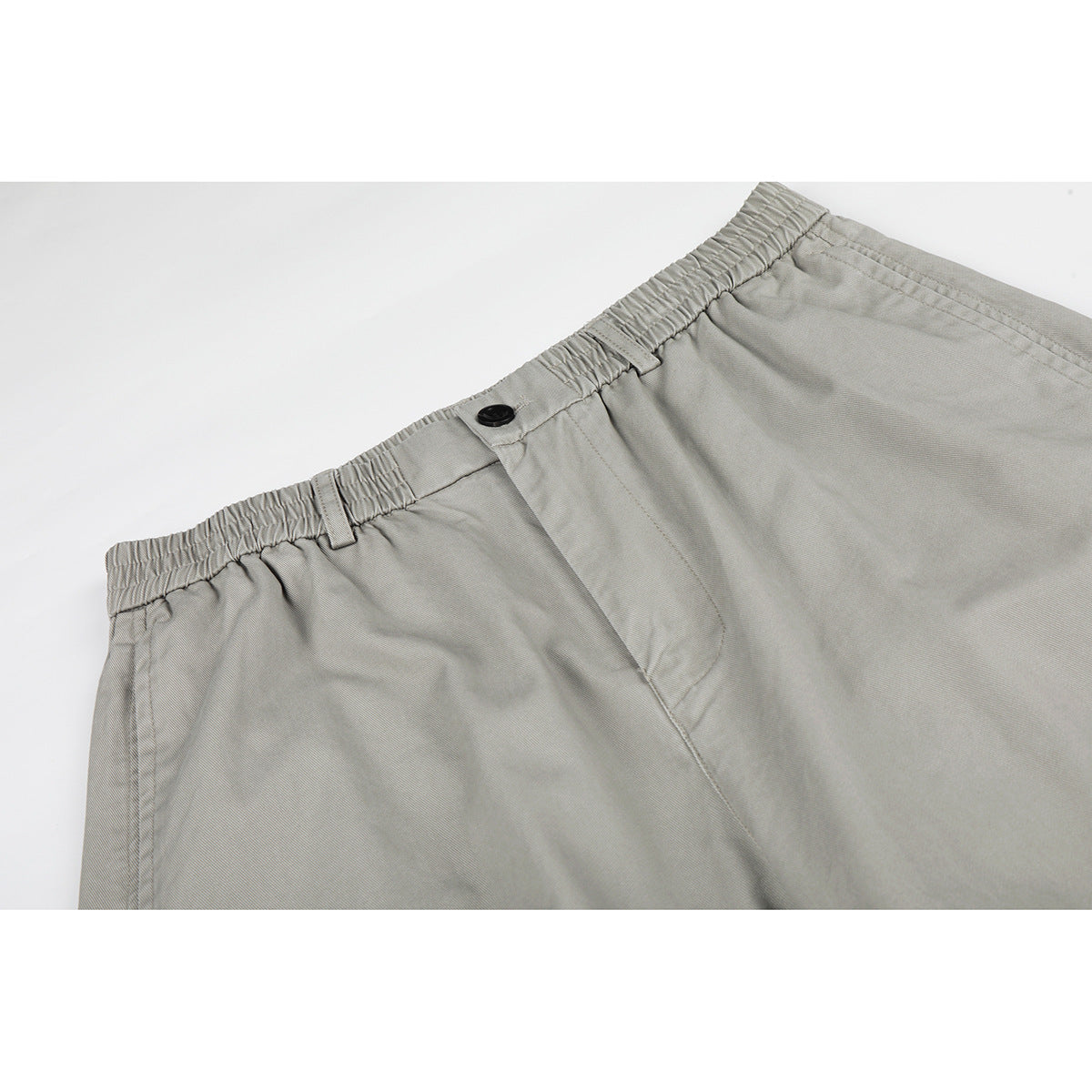 Close-up of light gray trousers showing the elastic waistband, belt loops, black button, and front fly.