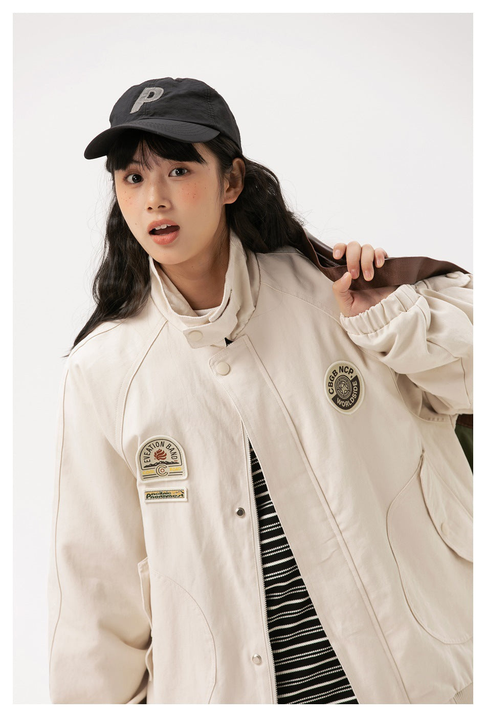 Model wearing a cream jacket with a high collar, snap-front placket, large pockets and decorative chest patches.